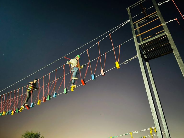 People crossing rope bridge at night adventure activity